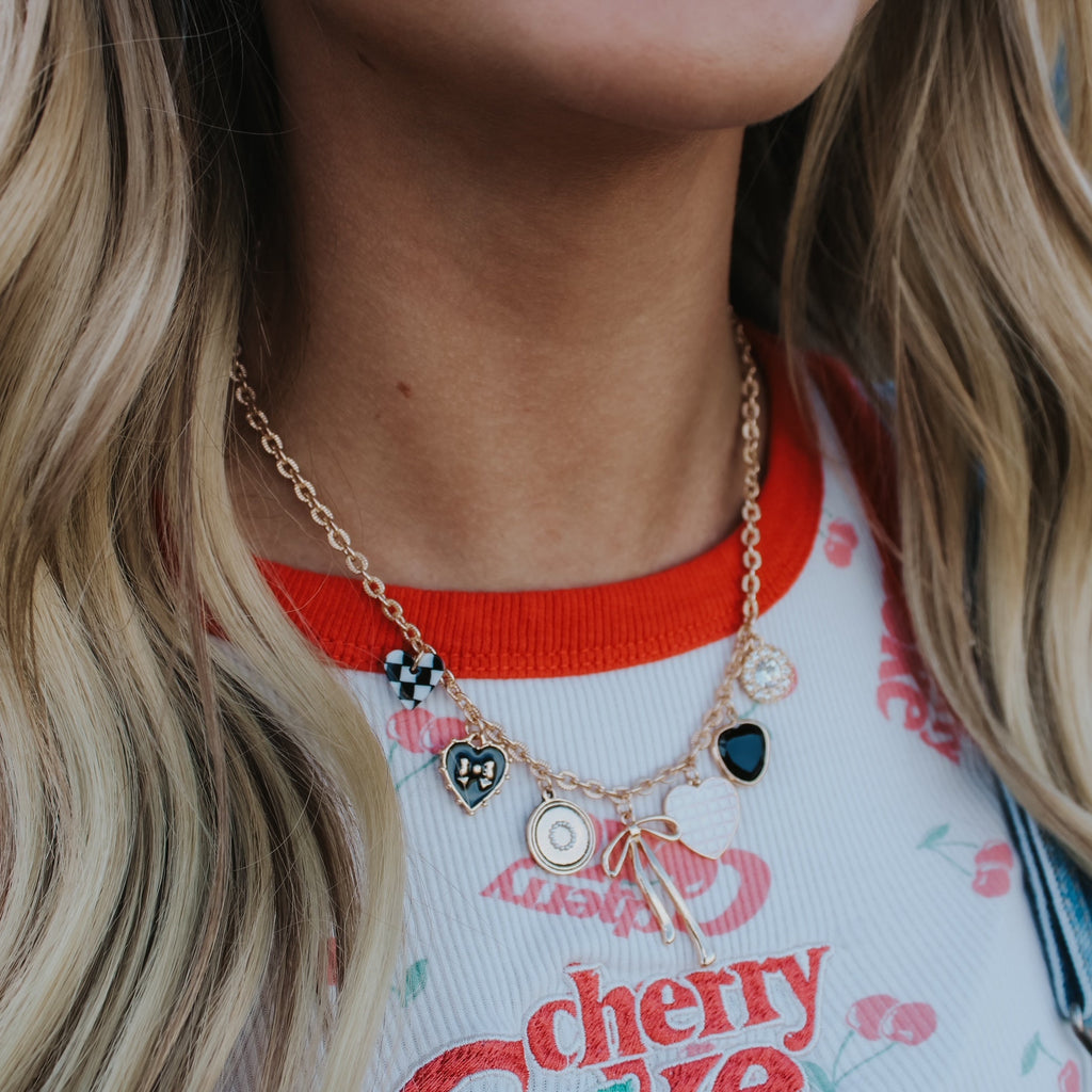 Person wearing a necklace with multiple charms against a blurred natural background charm necklace bow